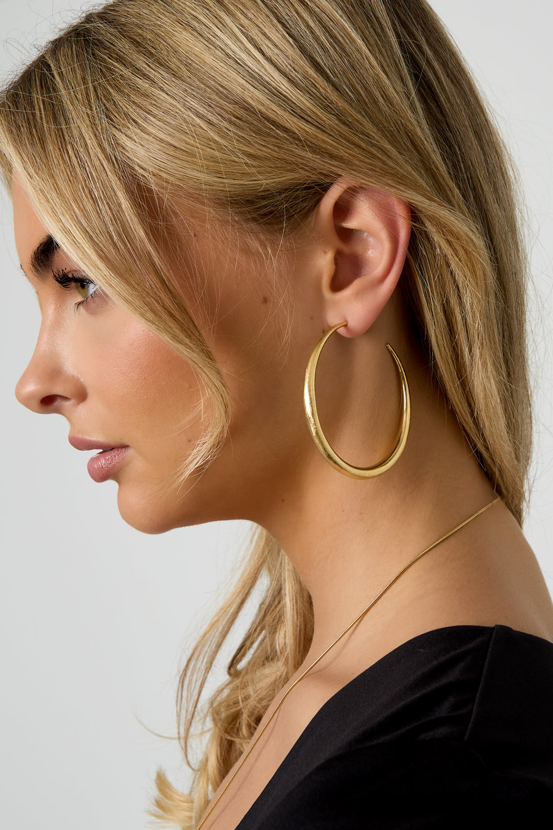 Gold oval-shaped Elena hoop earrings with a smooth finish worn in the ear from Sorea Fashion.